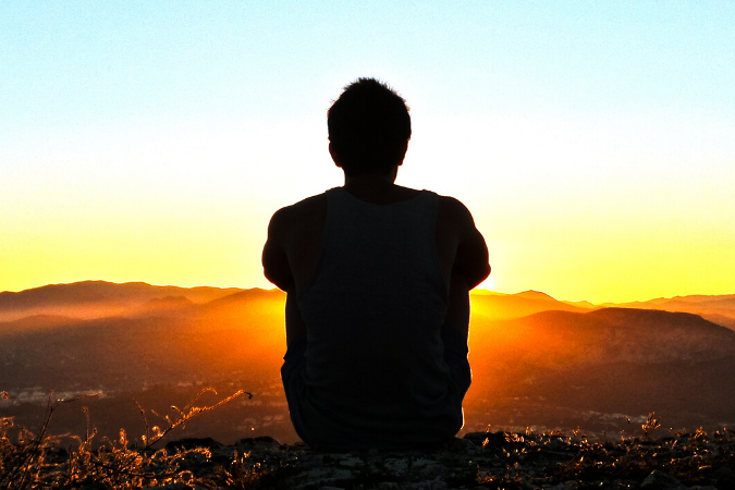 Outline of a man in a field sitting at dawn watching the sun set