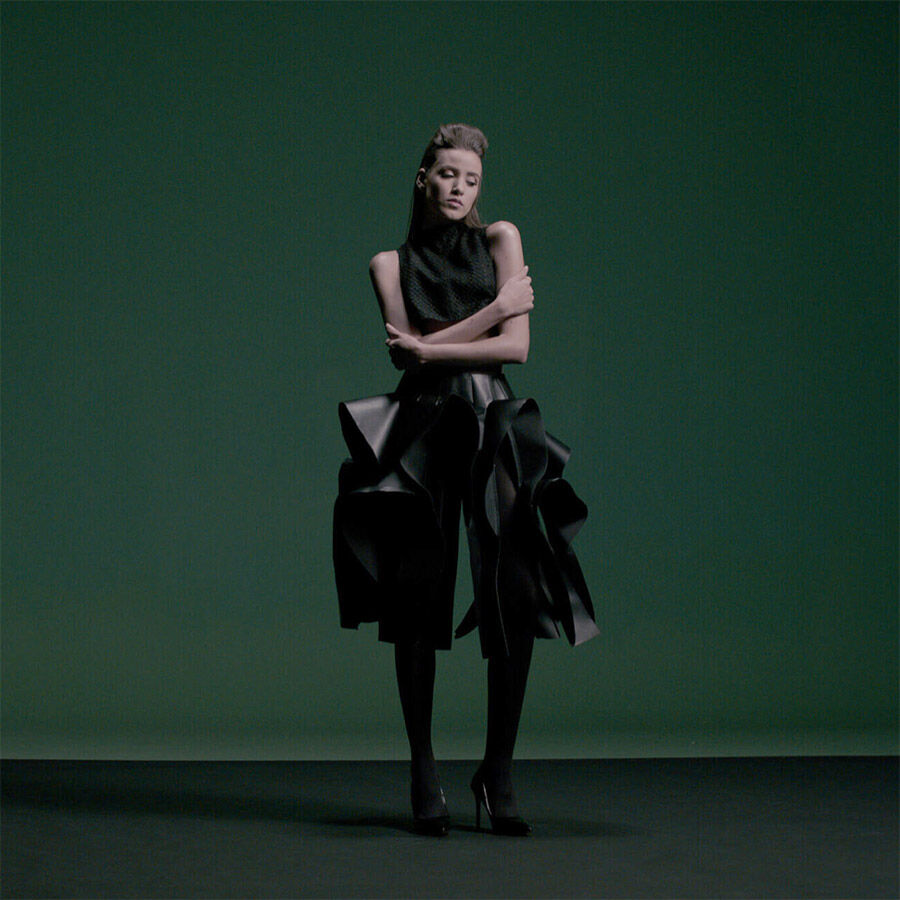 A woman in a black skirt standing in front of a green screen.
