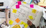 An overhead shot captures a brainstorming session on a white table. A central cloud shape with "What is PR?" is surrounded by colorful sticky notes with terms like "Promotion," "Campaign," and "Media Influencer Creation," as hands point and interact with magazines and phones.