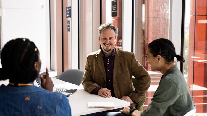 Three mature students discuss their work in a classroom