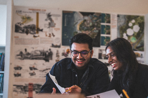 Two students talk and laugh whilst looking at work