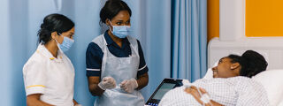 Two student nurses talking to patient lay on bed