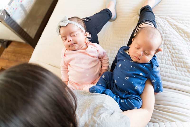 A woman sitting on a bed holding two babies