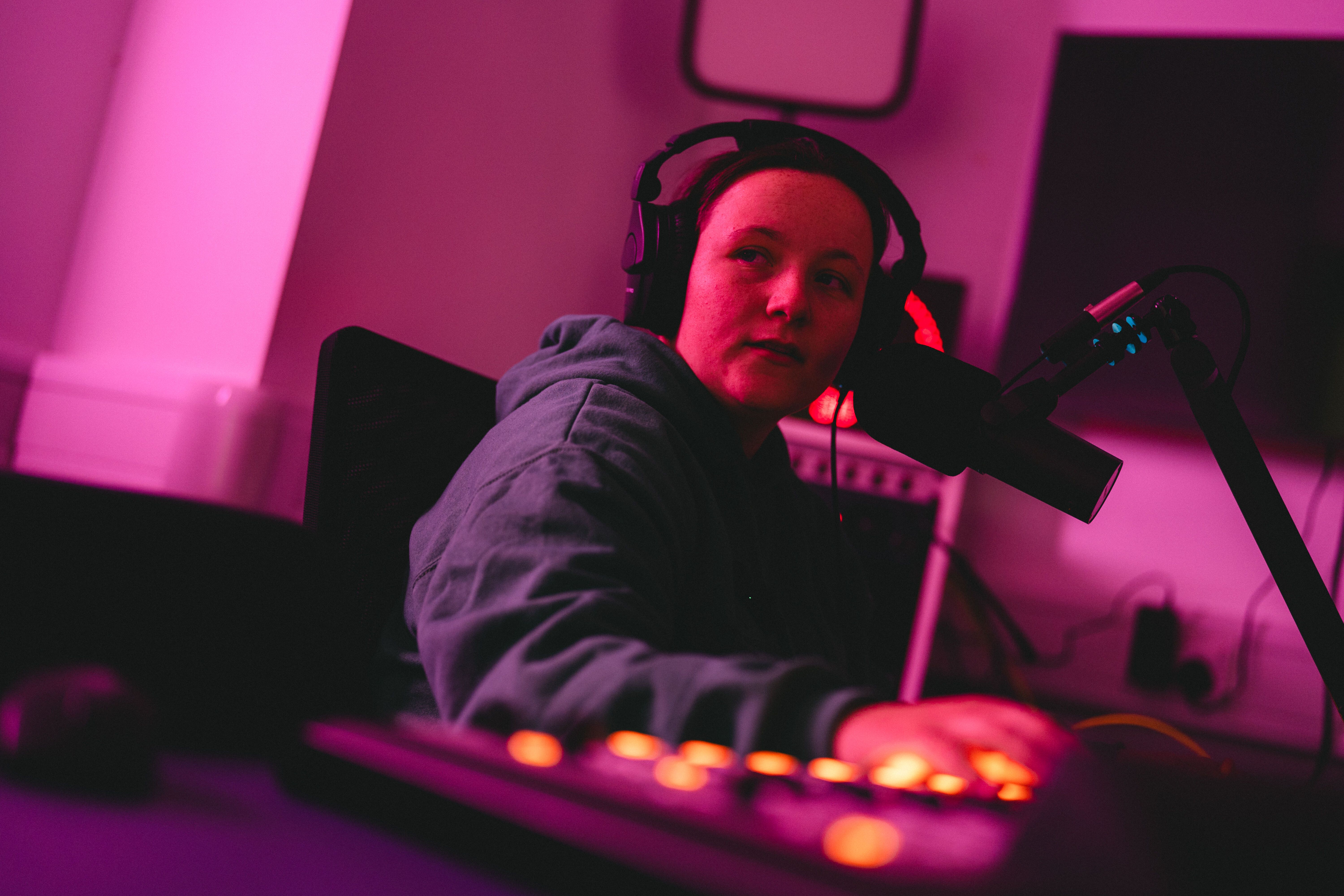 A student in a radio studio wearing headphones and using the mixing desk
