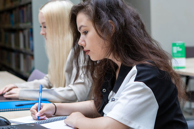 Students writing in notepads and typing on laptops in library