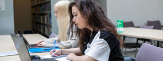 Students writing in notepads and typing on laptops in library