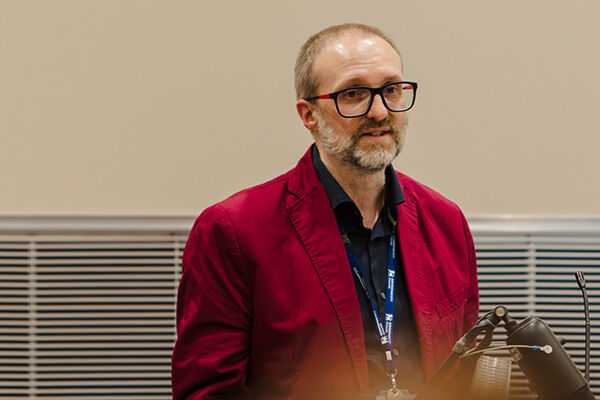 Peter, a man with short hair and glasses, wearing a red blazer 