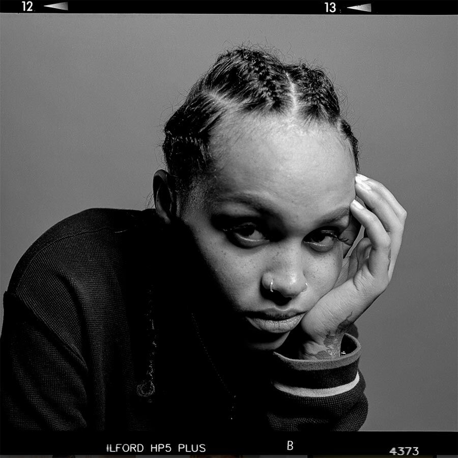 Black and white photography piece of person leaning on their hand and looking into the camera