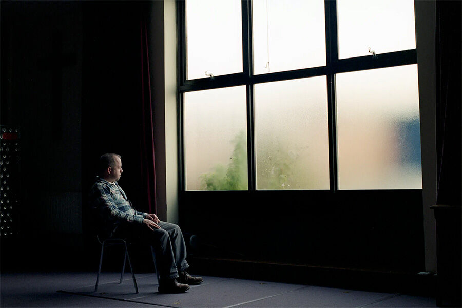 Photography piece of person sitting on a chair looking out of a large window