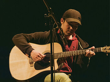Member of the Quench Arts community group playing guitar on stage