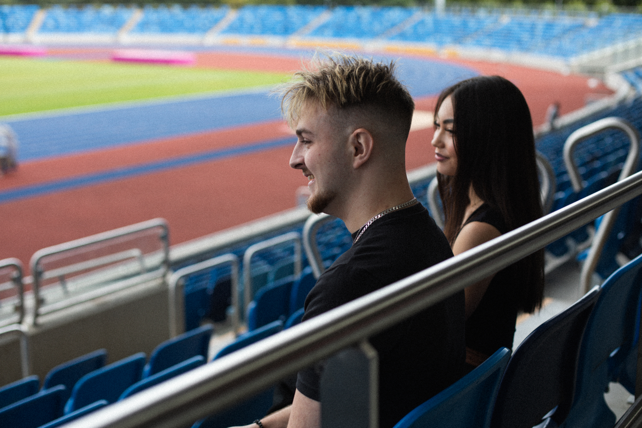 Two students sit in the stands of Alexander Stadium, looking out over the race track