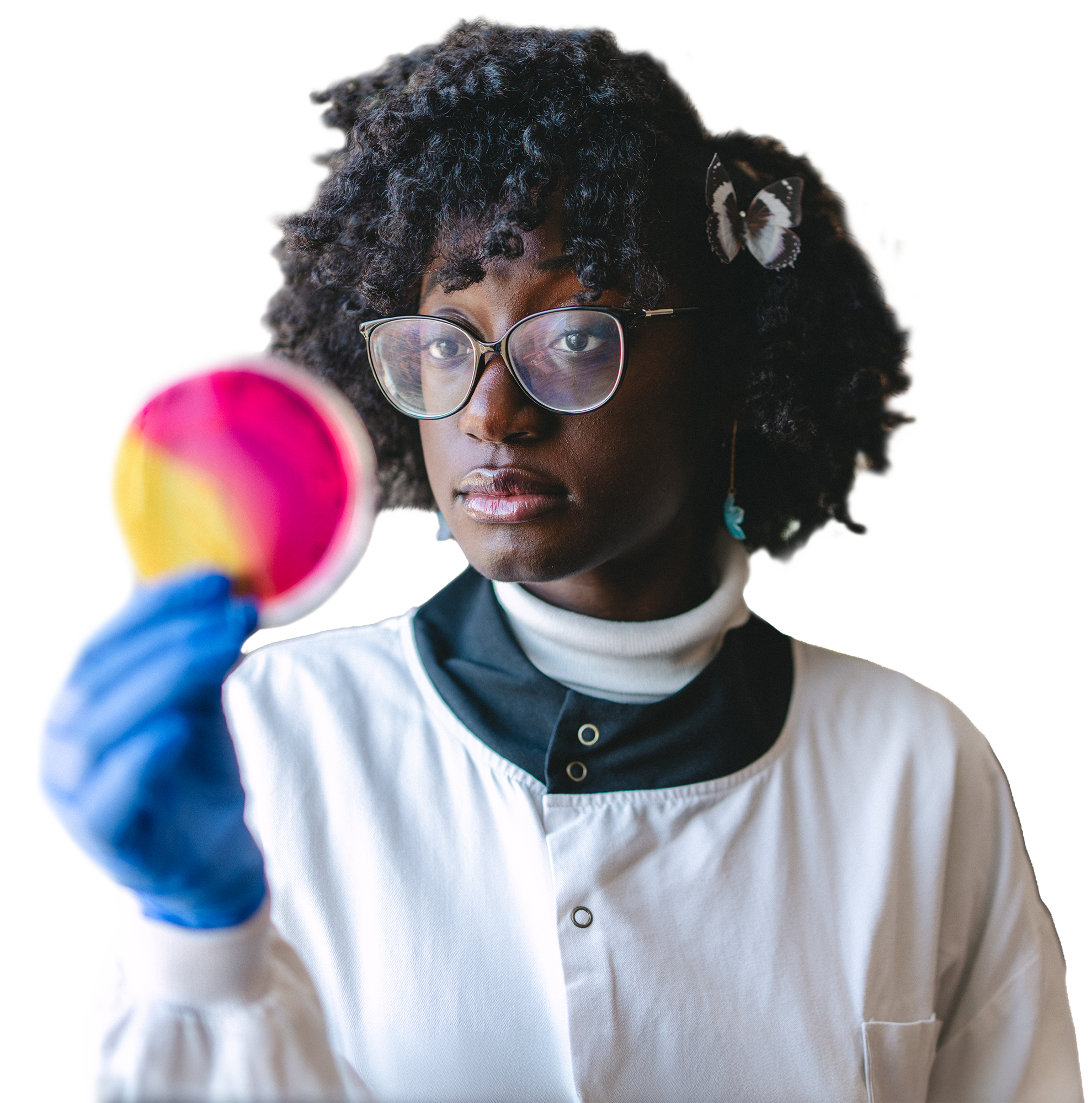 A biomedical scientist wearing safety glasses, a white lab coat and blue gloves, examining a colourful circular object held up in front of her.