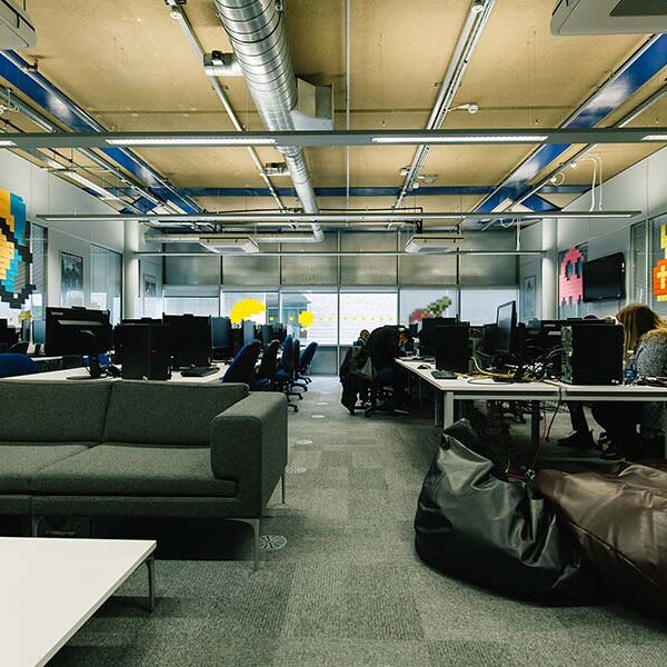 Interior view of a contemporary office with computer workstations, a grey sofa, beanbag chairs, and pixel art decorations on the walls.