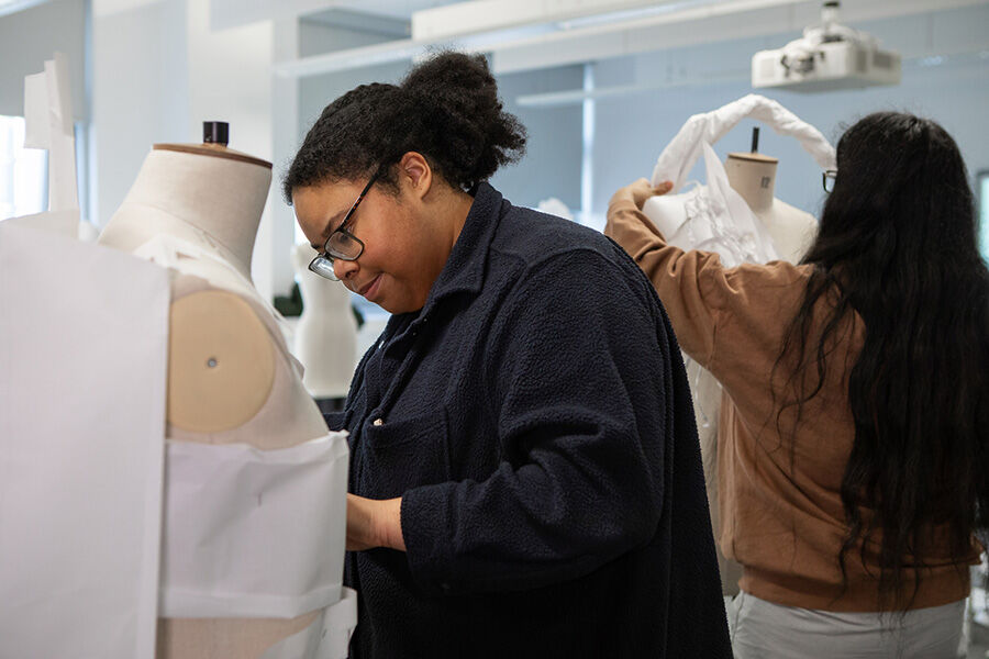 Two students working on mannequins with twisted white fabric