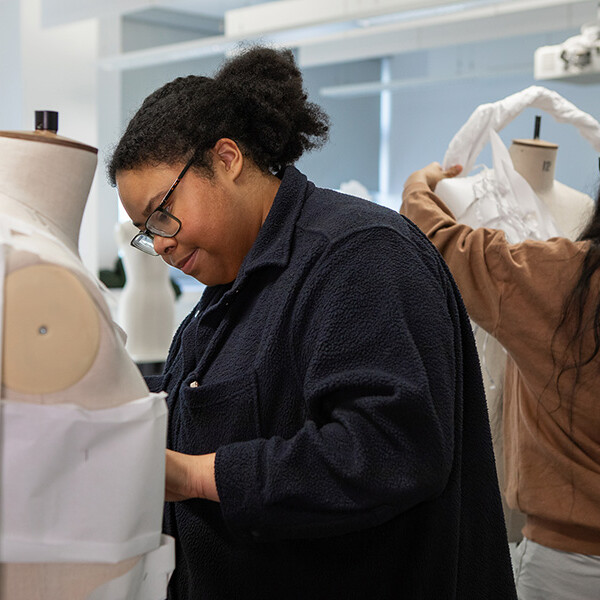 Two students working on mannequins with twisted white fabric