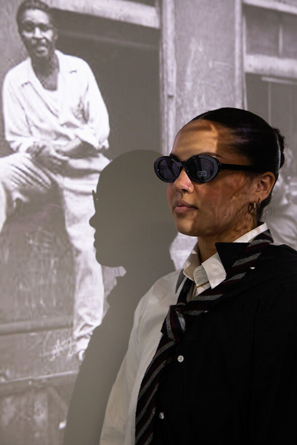 Female model in sunglasses and half white, half black suit in front of photo