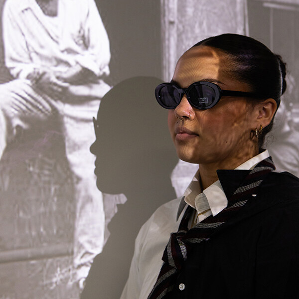 Female model in sunglasses and half white, half black suit in front of photo