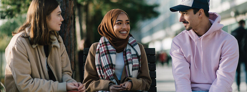 3 students are sat outside on campus, near the Millennium Point building