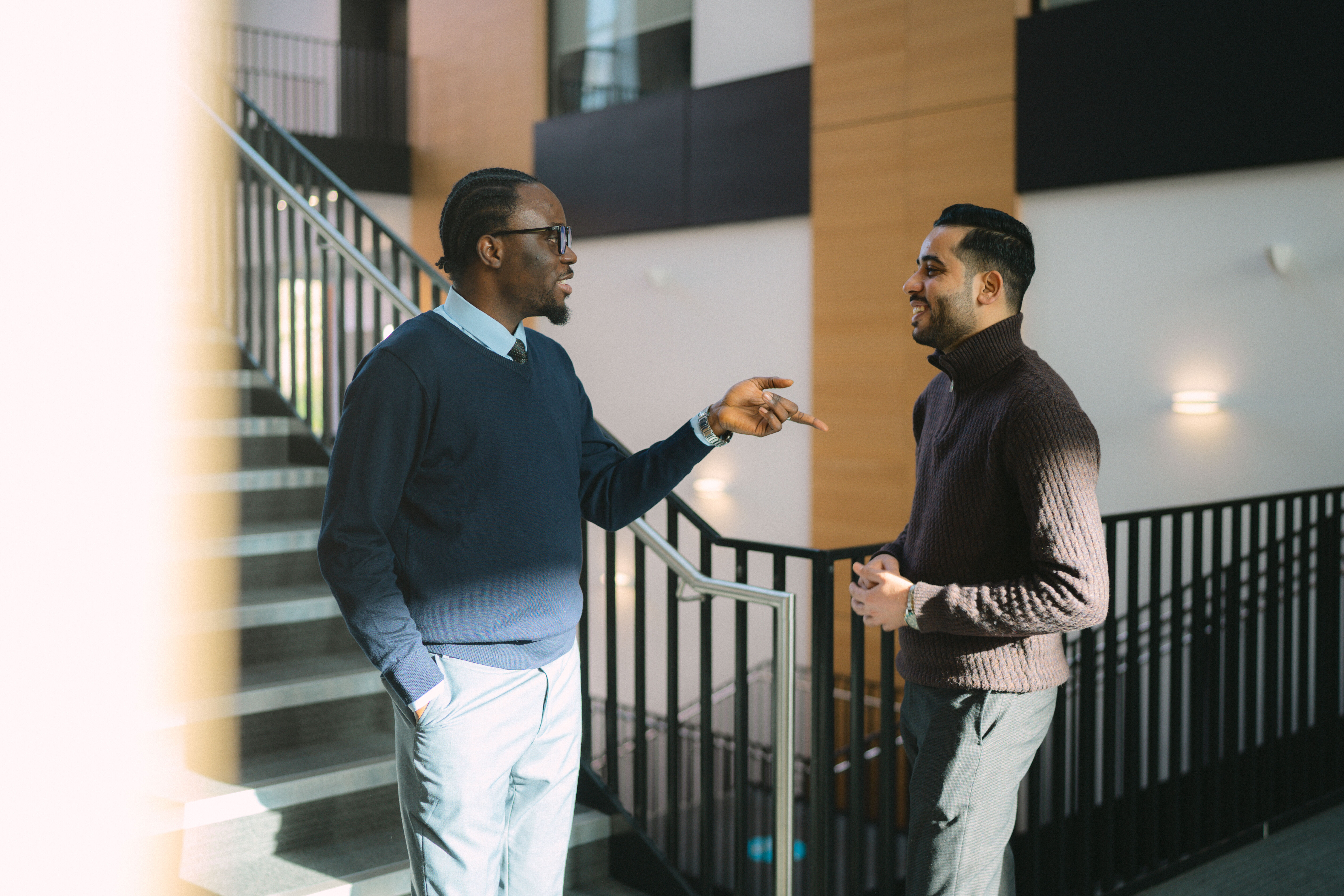 Two postgraduate students standing on a stairway, laughing together. 