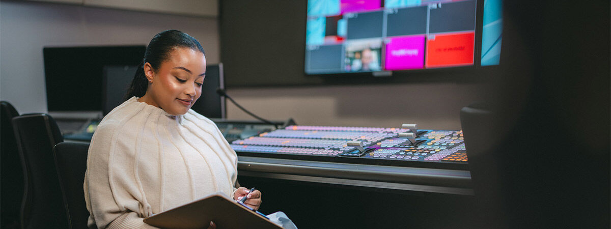 A student is sat in a recording and sound studio, holding a clipboard and pen
