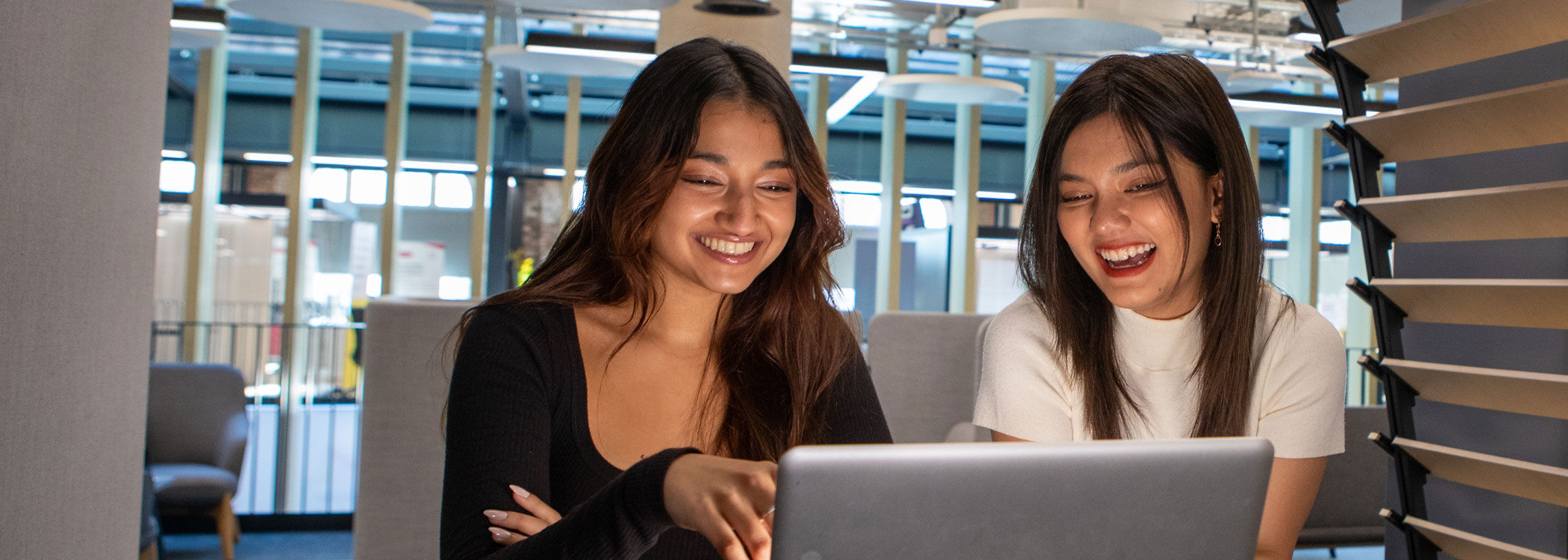 Two students laughing and smiling looking at laptop