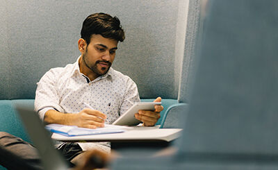 Student looking at ipad and writing in notebook