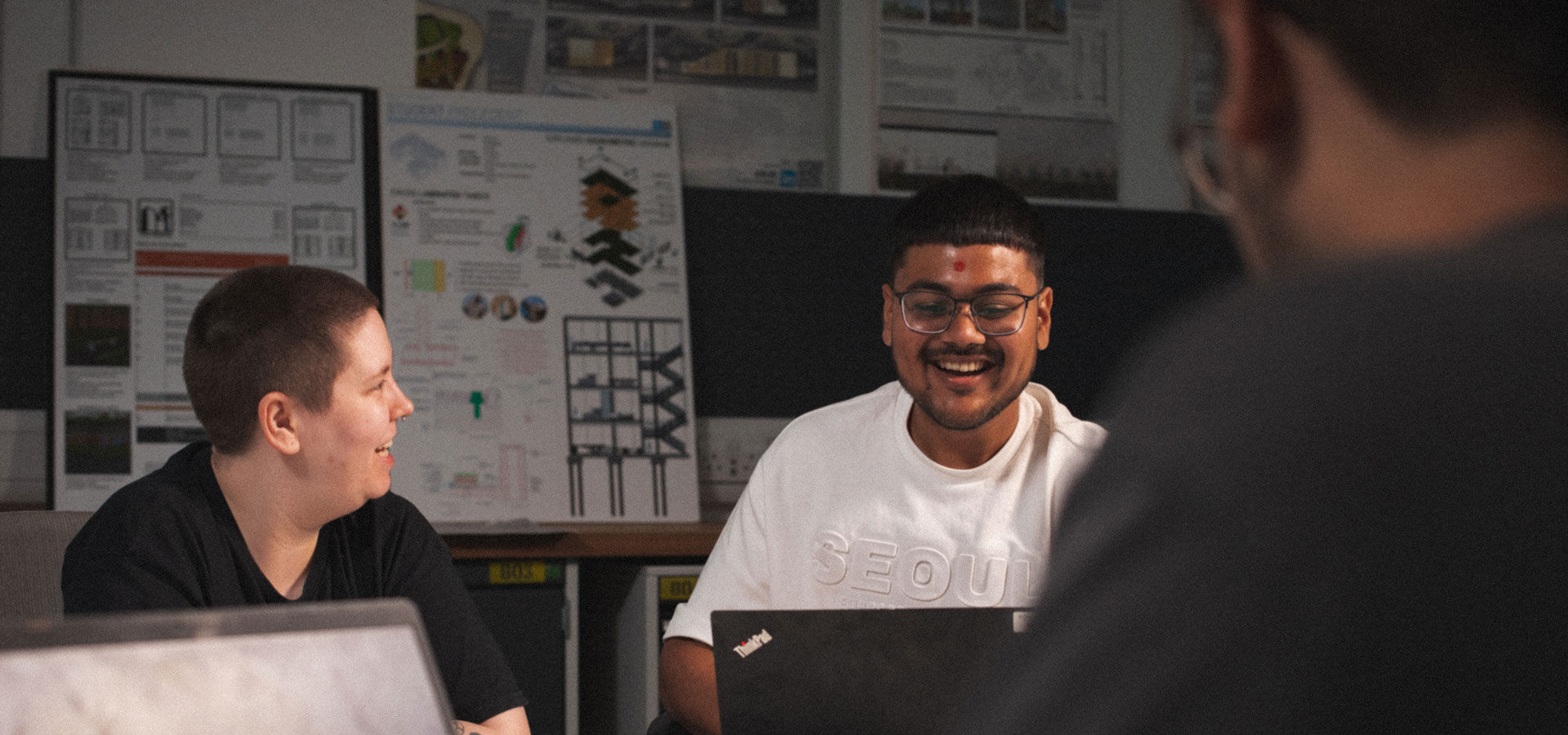 Three students talk whilst working on their laptops