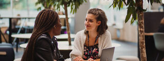 Two students sat at a table in the campus foyer having a conversation.