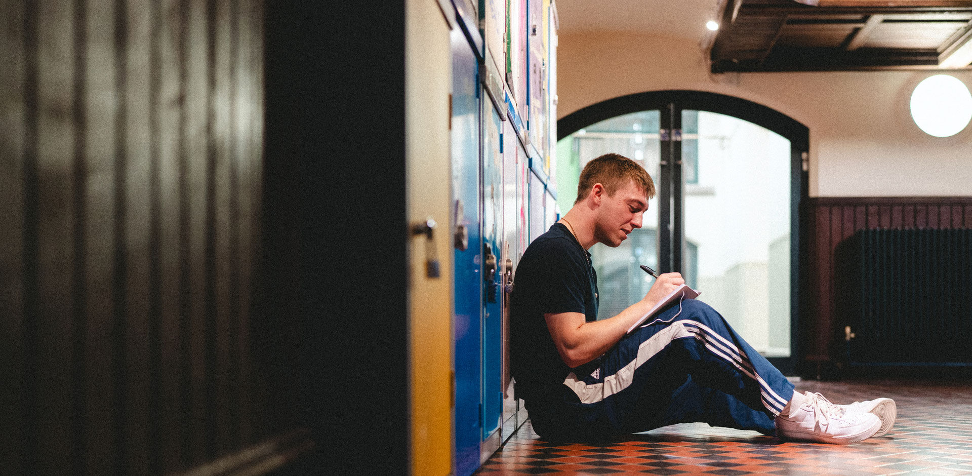 A student sits on the floor writing in their notebook at the School of Art
