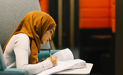 Student reading from a text book and writing on a notepad.
