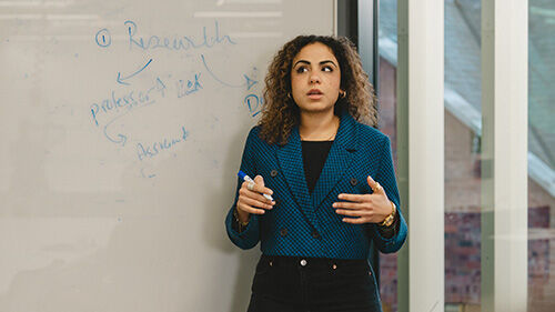 Woman with curly hair presenting by a whiteboard