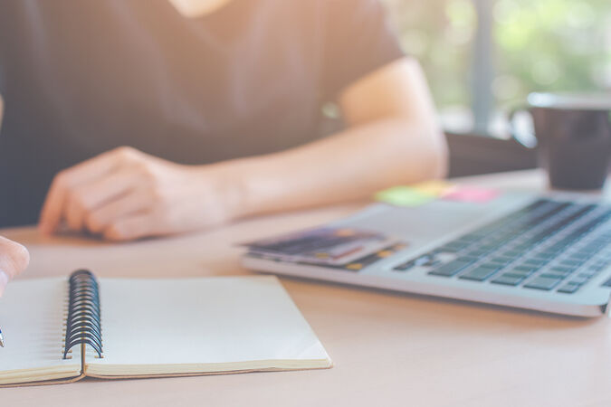 Person writing in a notebook next to a laptop computer