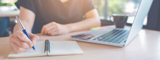 Person writing in a notebook next to a laptop computer